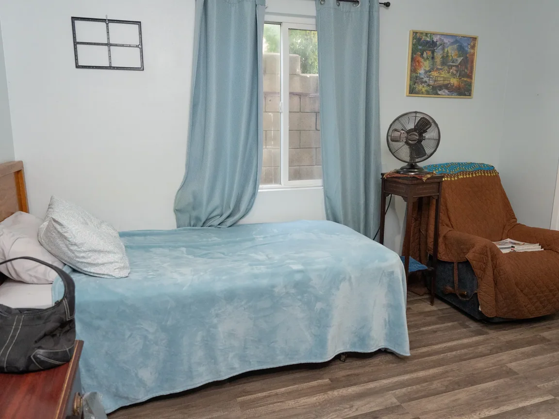 Comfortable resident bedroom with blue coordinated bedding, natural lighting, and armchair seating area